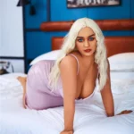Nimaya Sex Doll 156 cm IronTech Doll TPE en robe rose, posée à quatre pattes sur un lit.