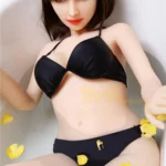 Séraphine Sex Doll 155 cm IronTech Doll TPE dans un bain, bikini noir, pétales jaunes.
