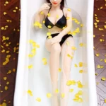 Séraphine Sex Doll 155 cm allongée dans une baignoire avec pétales jaunes, en lingerie noire.
