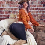 Velena Sex Doll 156 cm IronTech Doll en tenue western, posée de profil sur fond de briques.