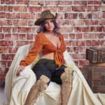 Velena Sex Doll 156 cm IronTech Doll TPE assise, chapeau et bottes, fond mur de briques.