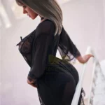 Velora Sex Doll 159 cm IronTech Doll en robe noire, vue de profil, sur un lit.