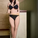 Zélie Sex Doll 157cm IronTech en lingerie noire, debout près d'un meuble, cheveux bruns.