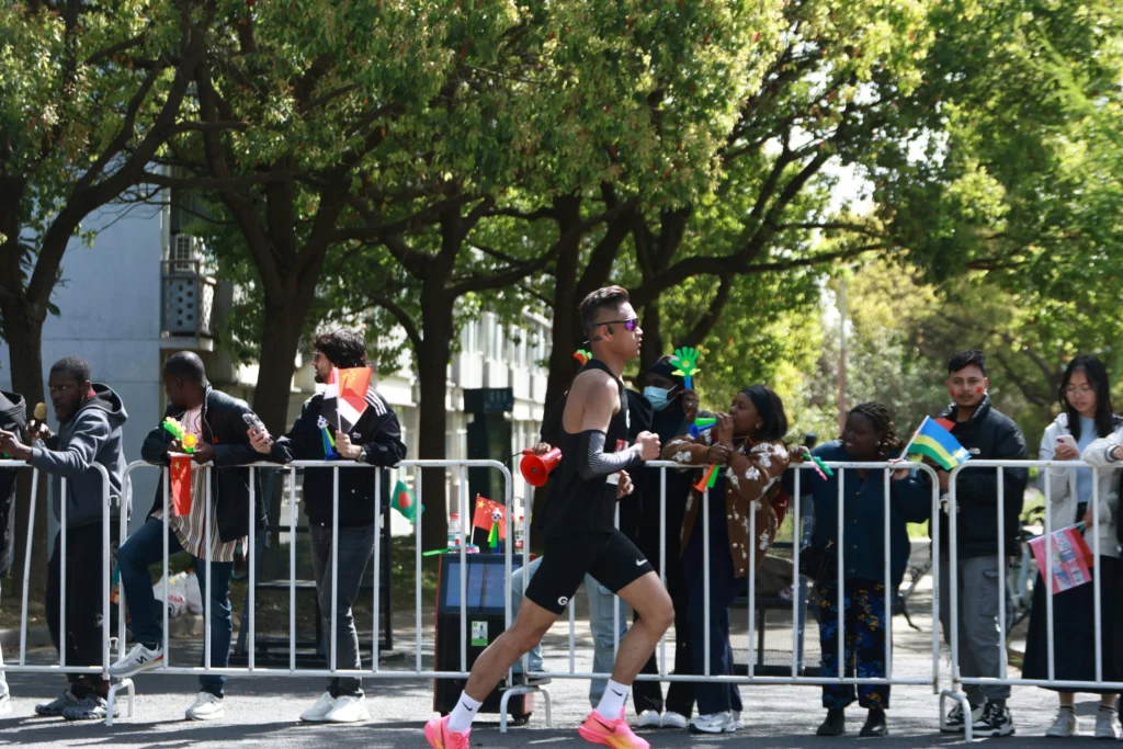 Coureur participant à une course urbaine entouré d'arbres verts et de spectateurs encourageants