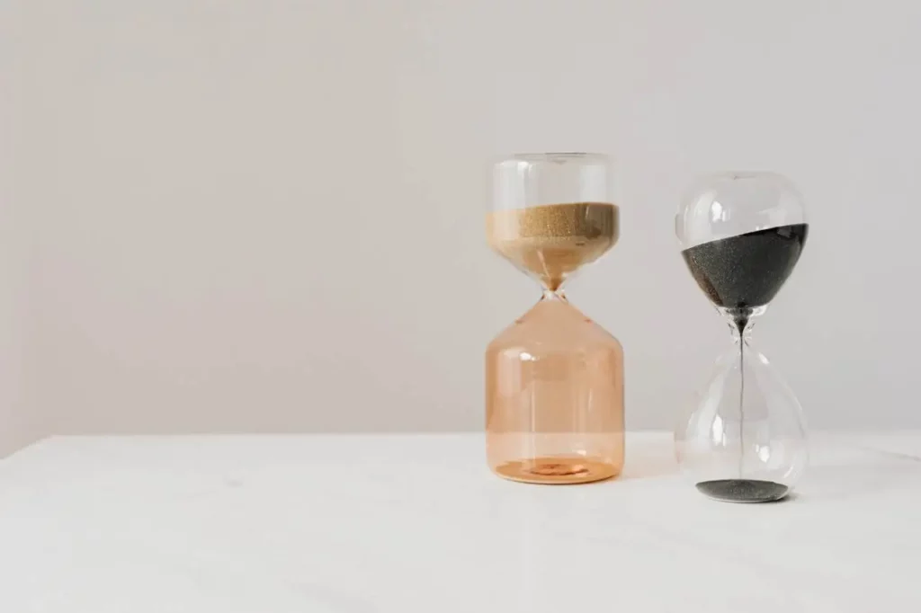 Deux sabliers très différents posés sur une table blanche, représentant le contraste des solutions pour l'éjaculation précoce et la gestion du temps dans les rapports sexuels.