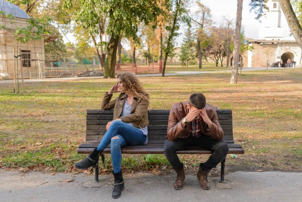 Un homme assis sur un banc se prend la tête pendant qu’une femme est assise à côté de lui, illustrant l’anxiété de performance sexuelle dans le couple