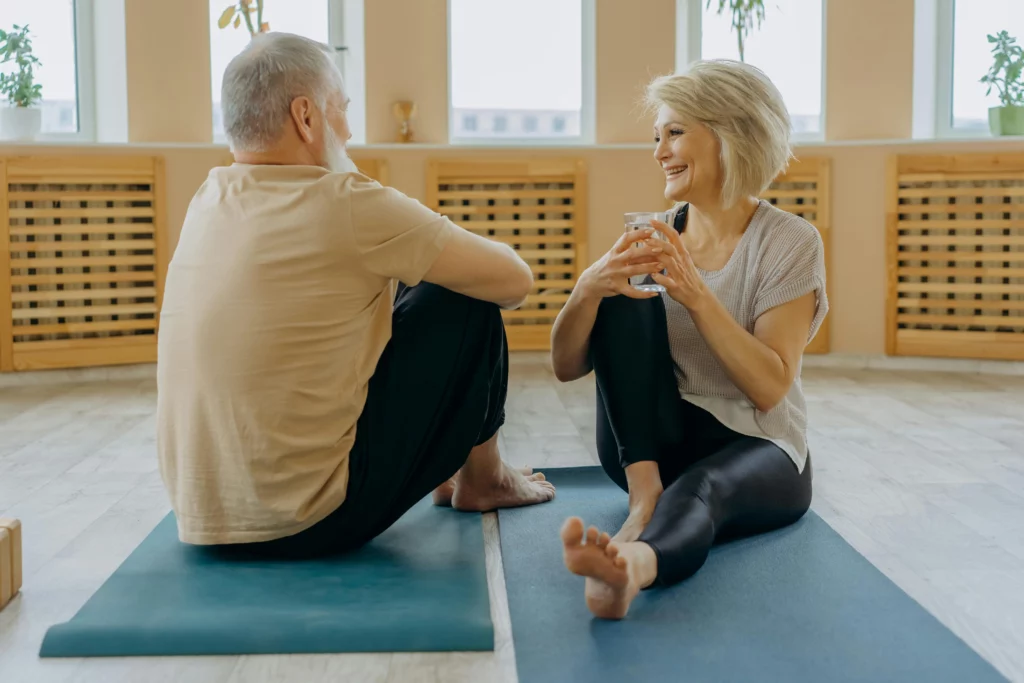 Homme et femme seniors assis sur des tapis de yoga, discutant après une séance de bien-être, favorisant la santé érectile masculine