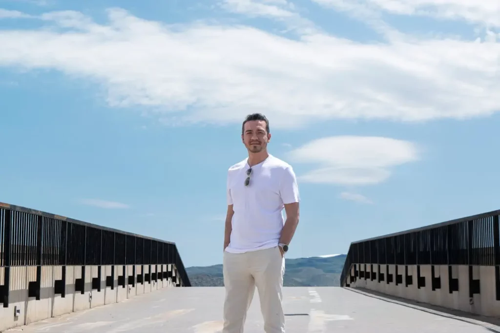 Homme serein en t-shirt blanc, lunettes de soleil accrochées, mains dans les poches, dehors, illustration de confiance et de sérénité