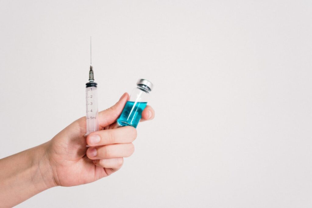 Main tenant un flacon contenant un liquide bleu et une seringue, symbolisant les traitements par injection PRP pour l’éjaculation précoce.