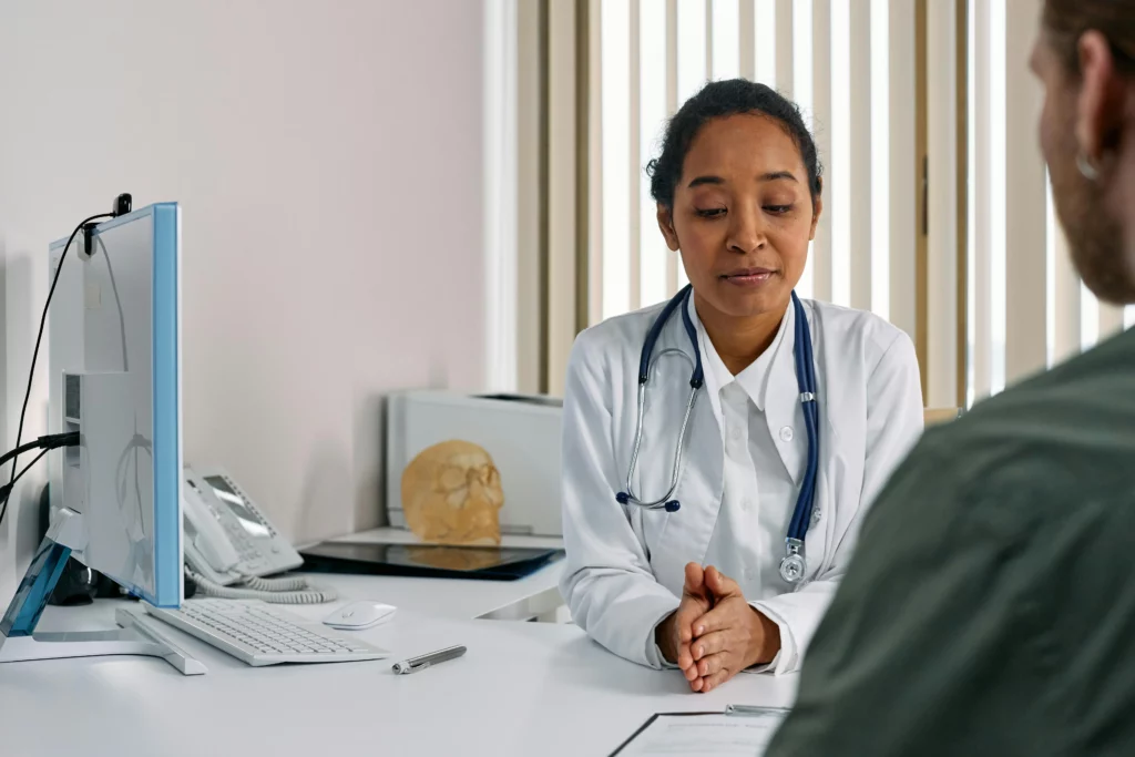 Une femme médecin en blouse blanche écoute attentivement un patient lors d'une consultation médicale en cabinet