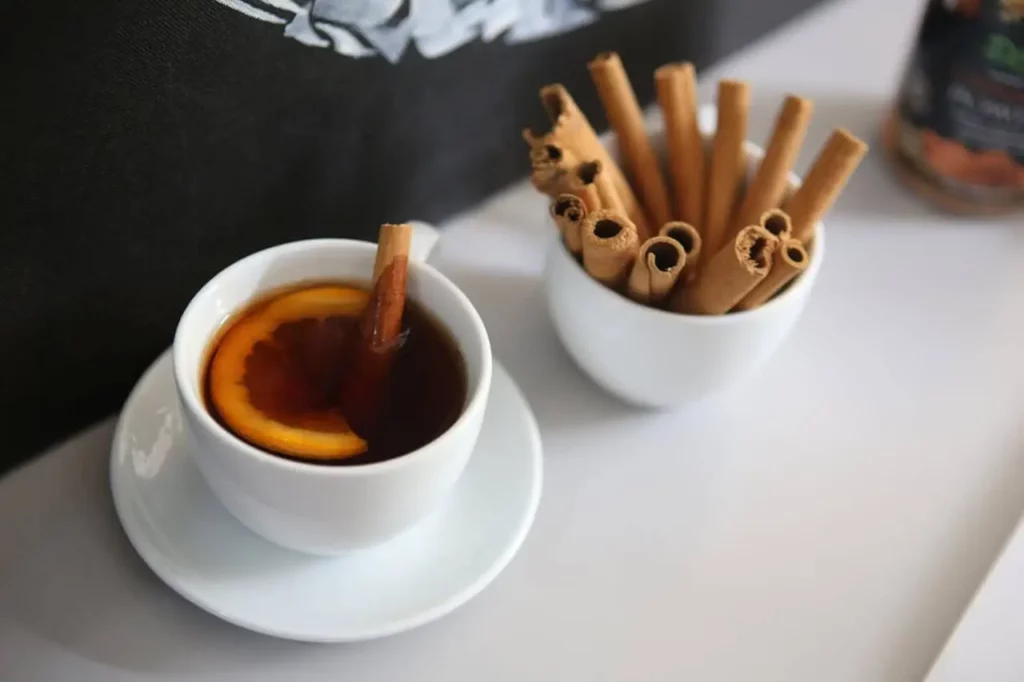 Tasse de tisane aphrodisiaque avec un bâton de cannelle, posée à côté d’un pot rempli de cannelle.