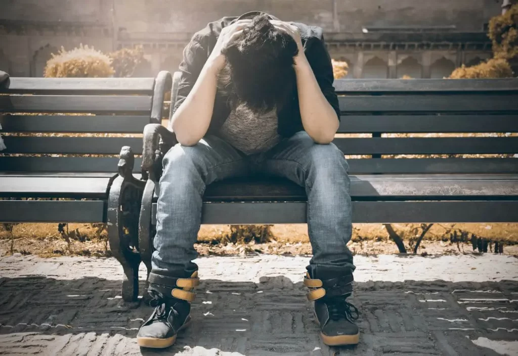 Un homme seul assis sur un banc public, la tête dans les mains, exprimant la détresse liée à la solitude amoureuse